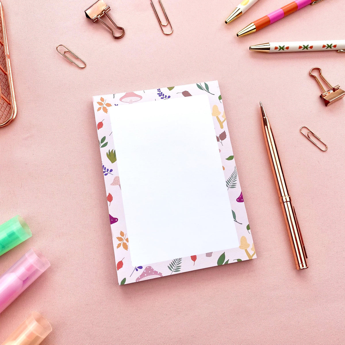 Autumn foliage-patterned notepad on a pink surface with stationery items