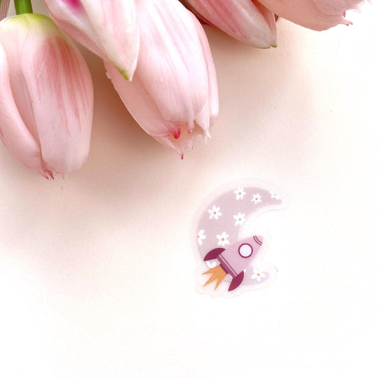 Decorative sticker with pink rocket and floral moon design on a white background