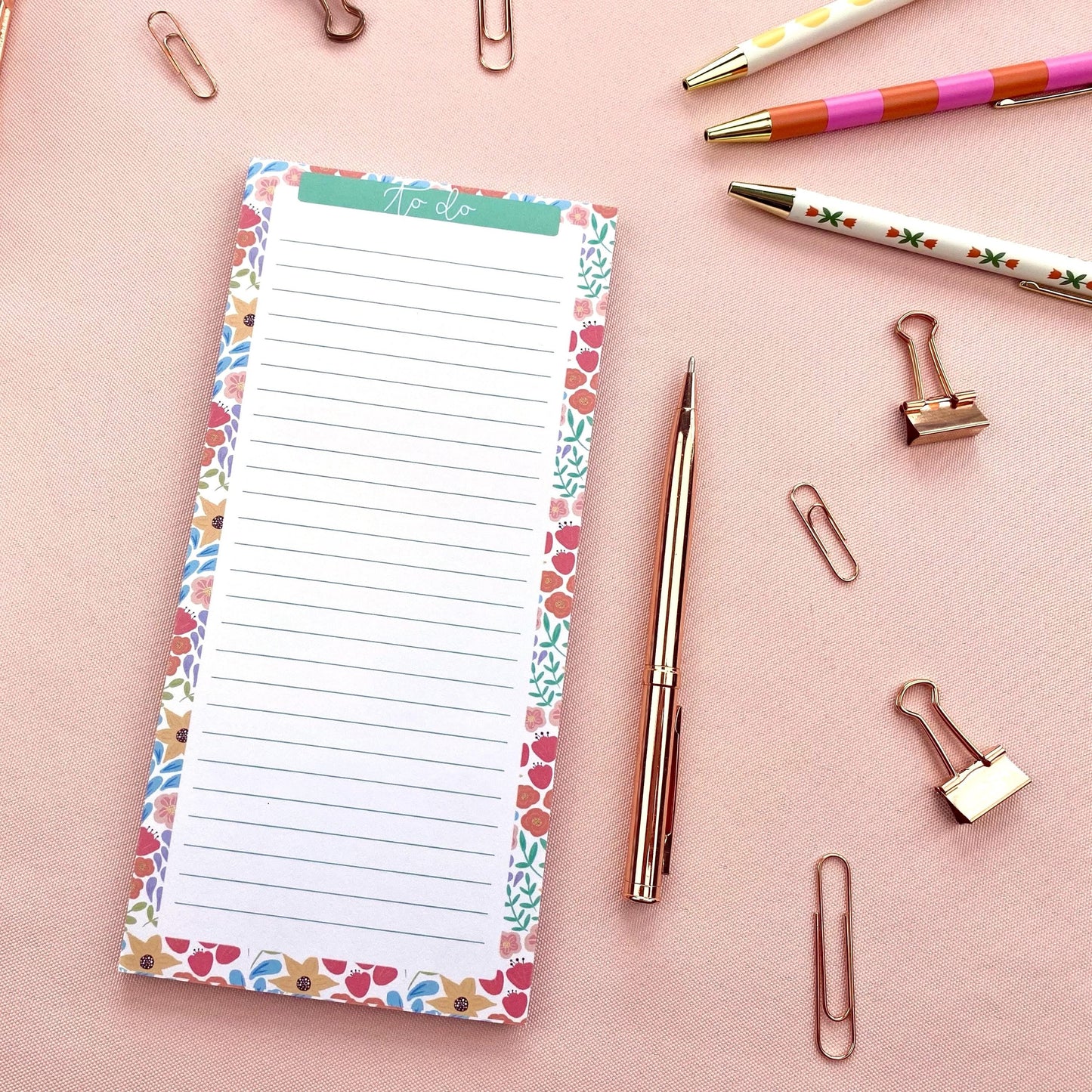 Floral-patterned notepad with pens and paper clips on a pink background