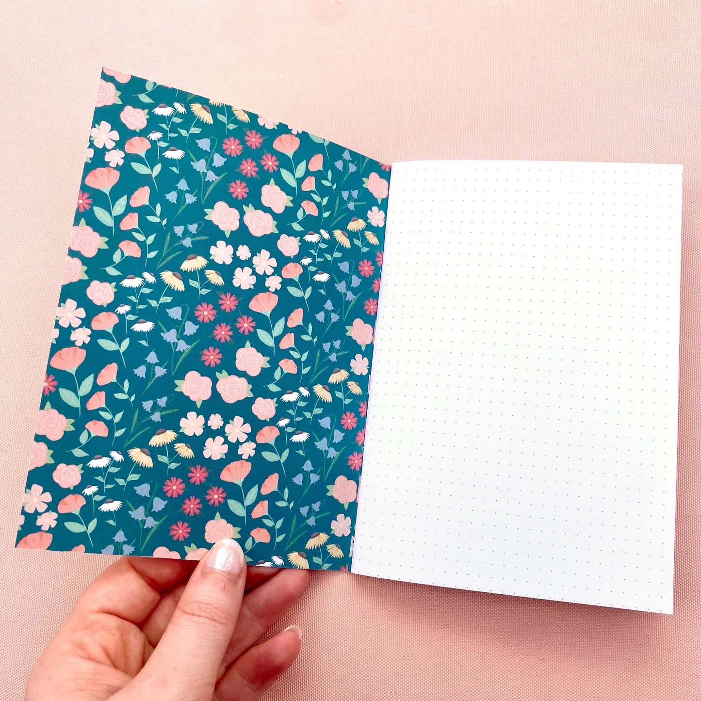 Floral patterned notebook cover held by a hand on a pink background