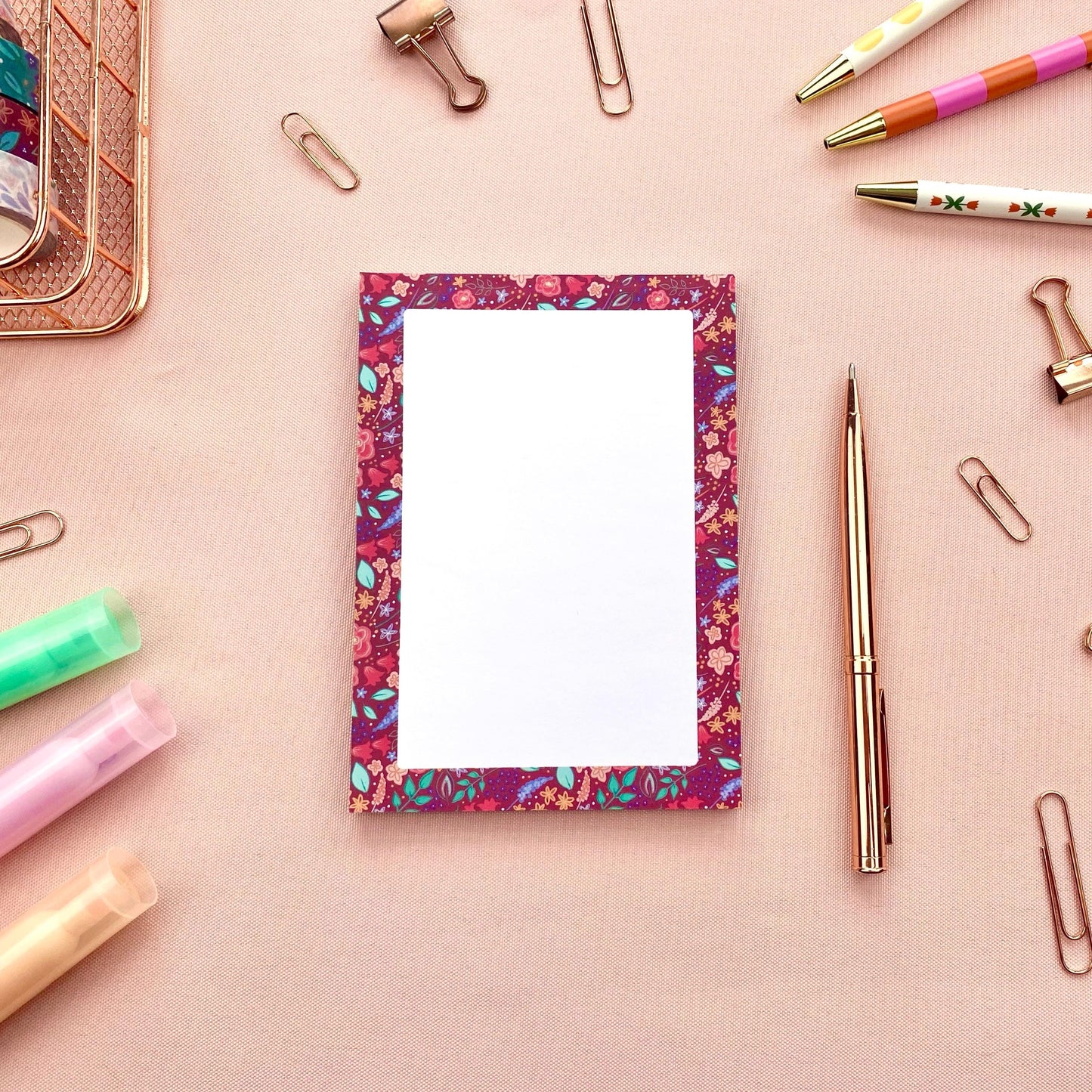 Floral-patterned notepad with stationery items on a pink background