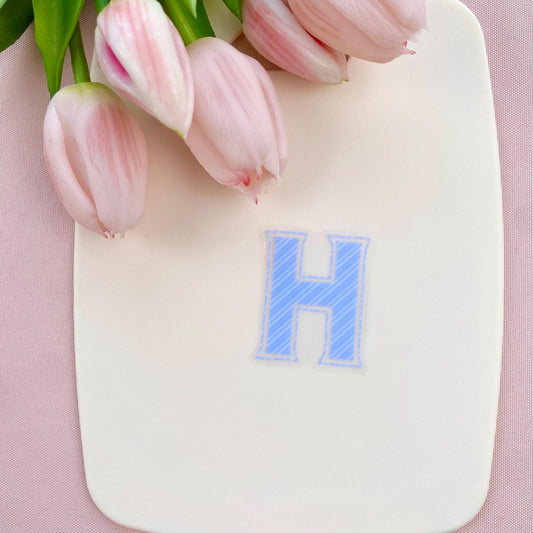 Blue striped letter 'H' sticker and pink tulips on a pink background