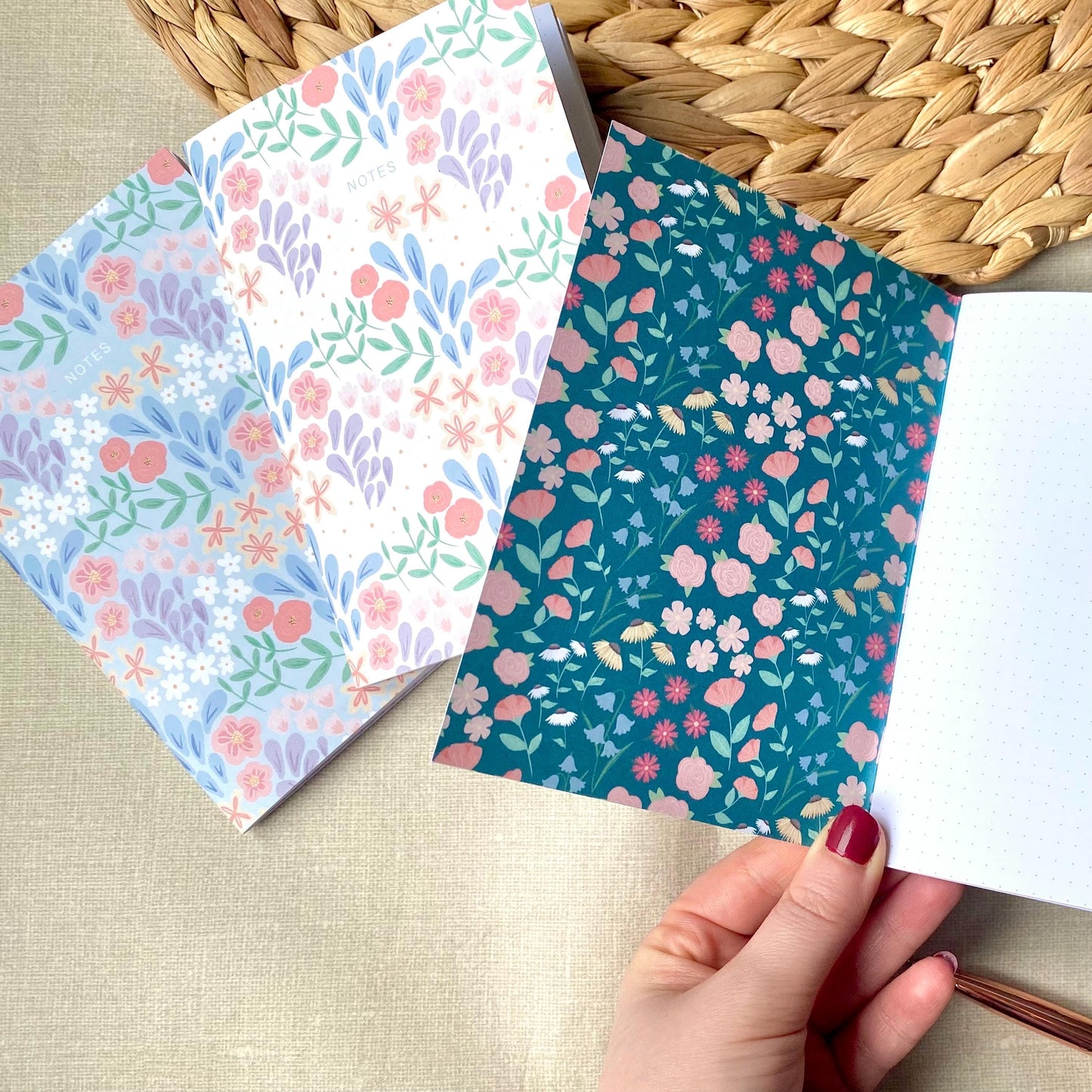 Two floral-patterned notebooks on a textured surface with a hand holding one of them.