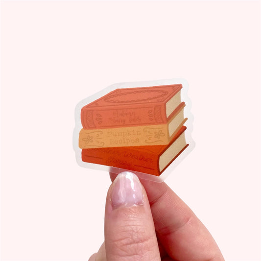Hand holding a sticker of three stacked books on a white background