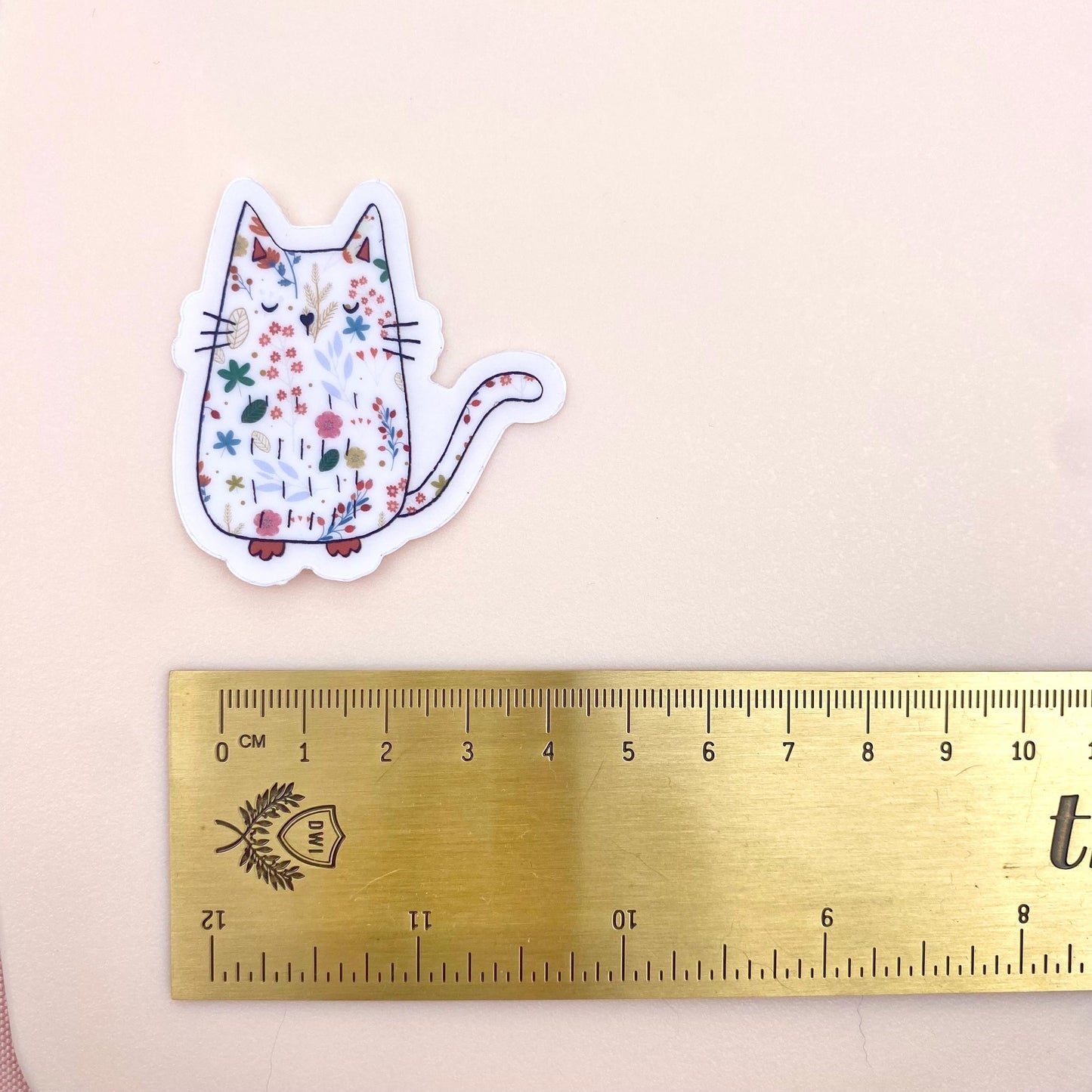 Sticker of a cat with floral patterns next to a ruler on a beige background