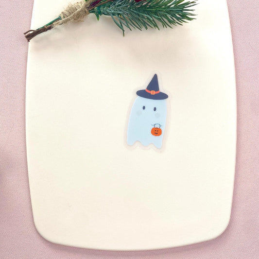 A sticker with a cartoon ghost wearing a witch hat and orange pumpkin on a pink background