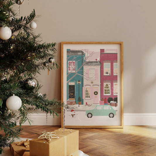 Framed artwork of colourful festive decorated houses on a wall next to a Christmas tree with decorations.