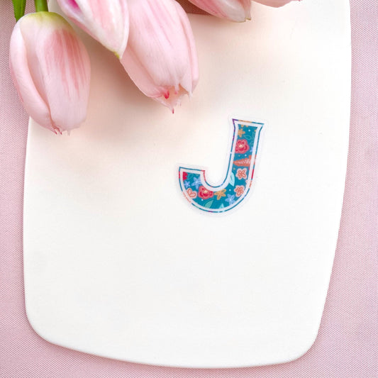 Colourful letter 'J' sticker on a pink background with tulips.