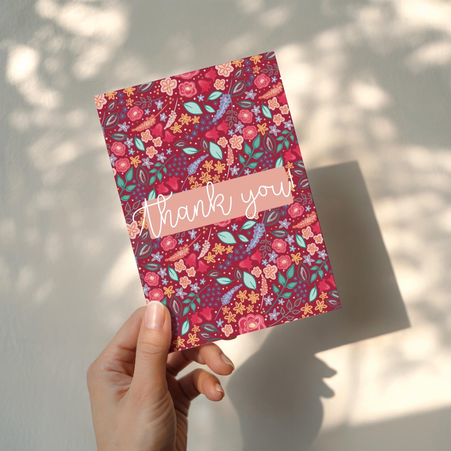 Floral patterned card with 'thank you' text held by a hand against a light background