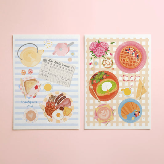 Two illustrated breakfast-themed art prints displayed side by side on a soft pink background. The left print has light blue and white stripes with drawings of a teapot, newspaper, toast, eggs, and bacon. The right has a yellow grid background with illustrations of a croissant, avocado toast, coffee, orange juice, waffles with berries and syrup, and a vase of flowers.