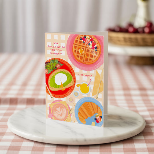 Colourful birthday greeting card with waffles and avocado toast design on a marble surface with a checkered tablecloth background