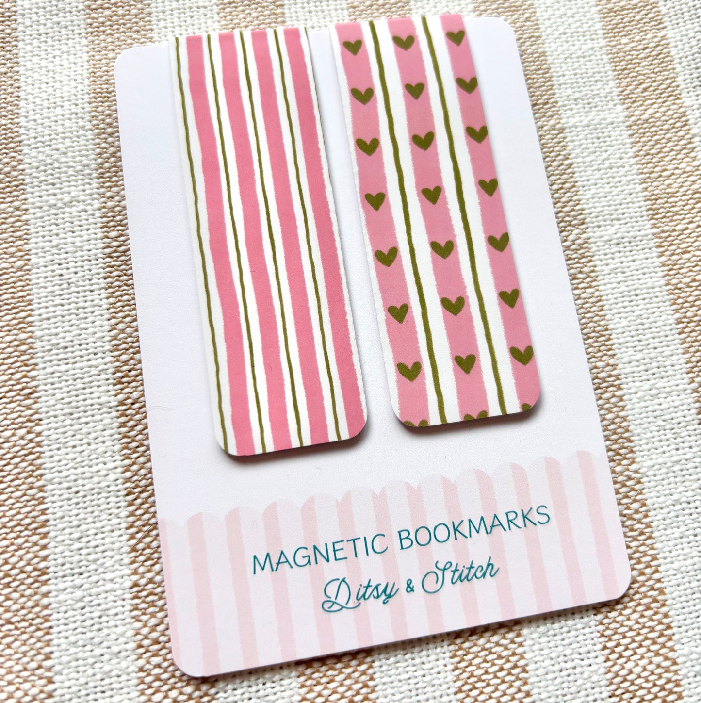 Two magnetic bookmarks with pink and green heart and striped patterns on a striped fabric background