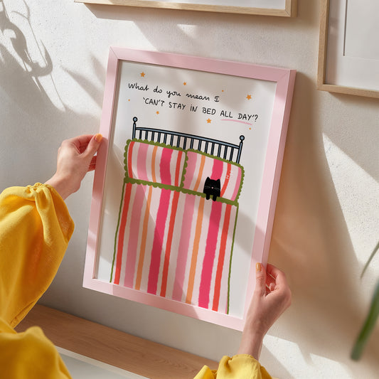 Person holding a framed illustration of a cat on a striped bed with text.