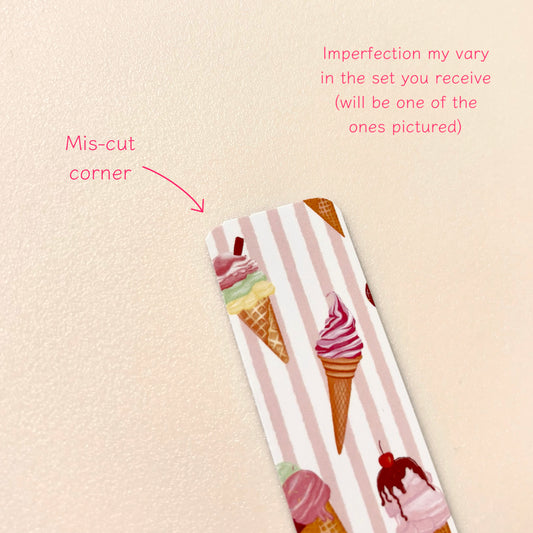 A close-up of a magnetic bookmark with pink and white vertical stripes and colourful ice cream cone illustrations, placed on a light beige textured background. Pink text and arrow call out a mis-cut corner and note variation in the set.