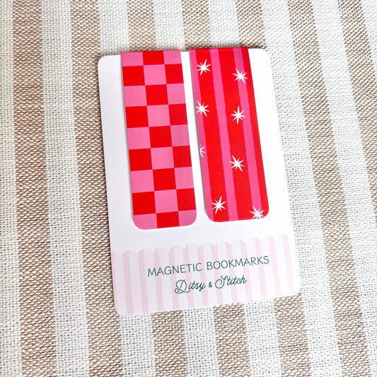 Two red and pink checkered magnetic bookmarks on a striped fabric background