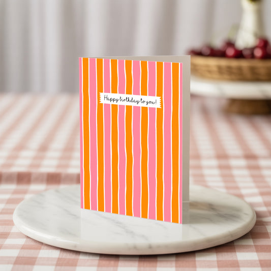 Striped birthday card with 'Happy birthday to you' text on a marble stand with a checkered tablecloth background.