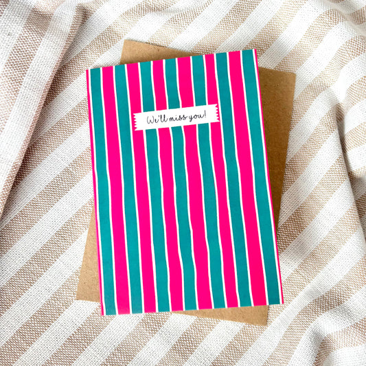Striped card with 'We'll miss you!' message on a textured fabric background
