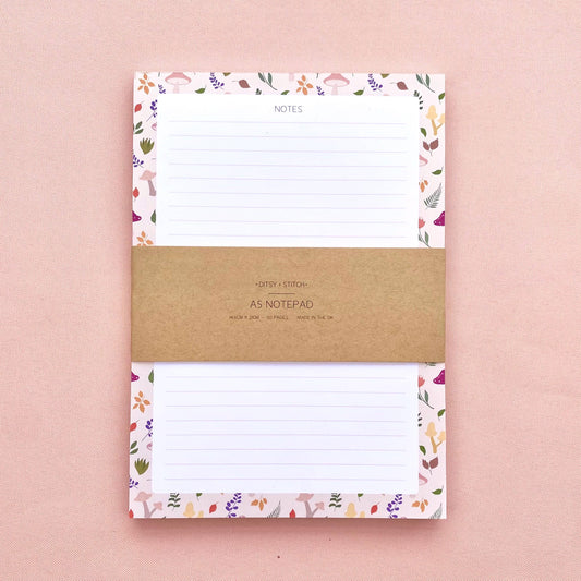 A lined notepad on a pink background, with a beige border patterned with autumn leaves and mushrooms