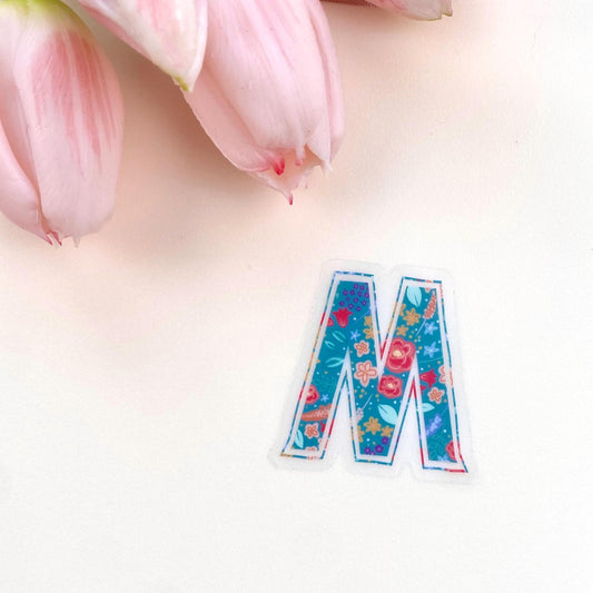 Colourful letter 'M' sticker with floral design on a light background