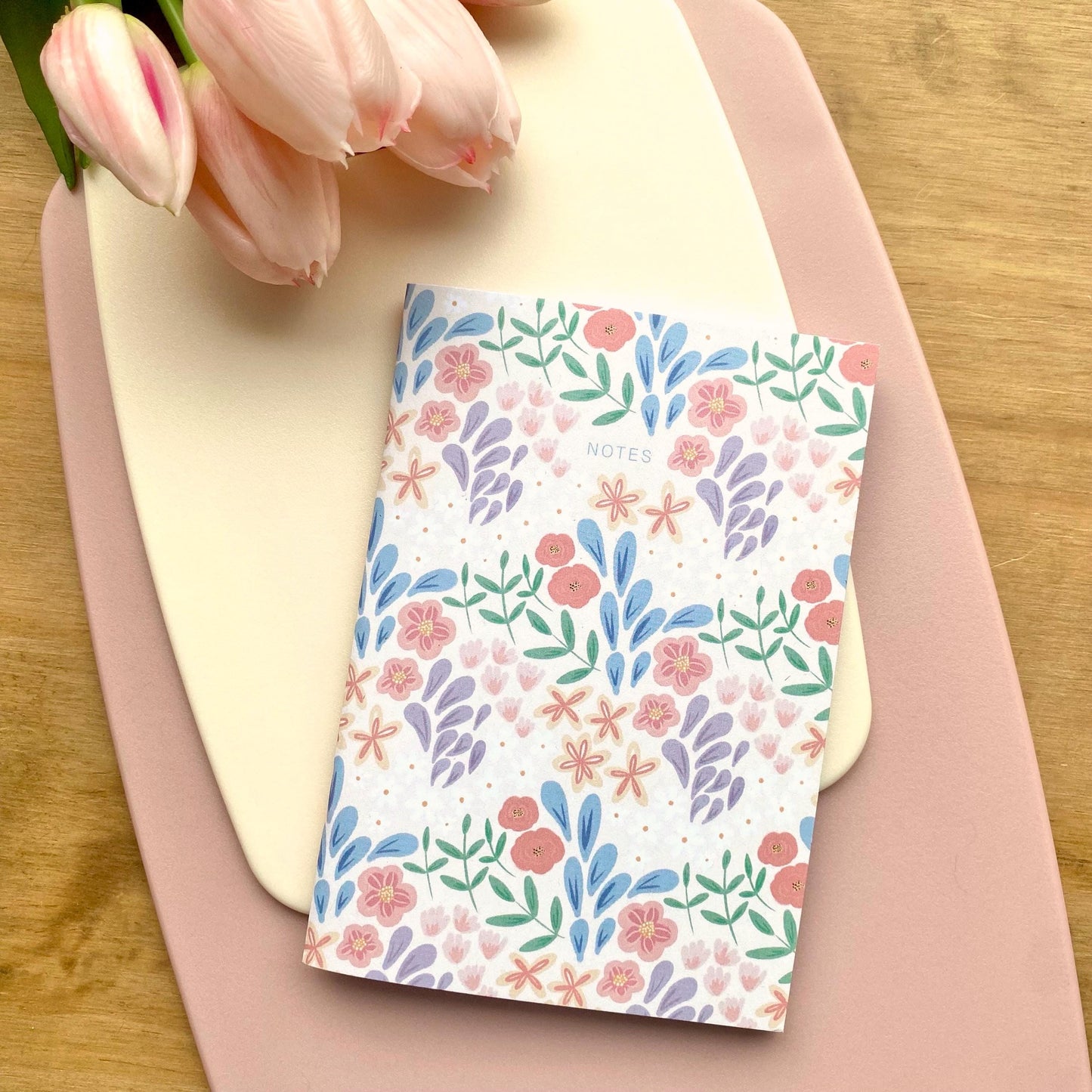 Floral notebook on a pink surface with tulips in the background