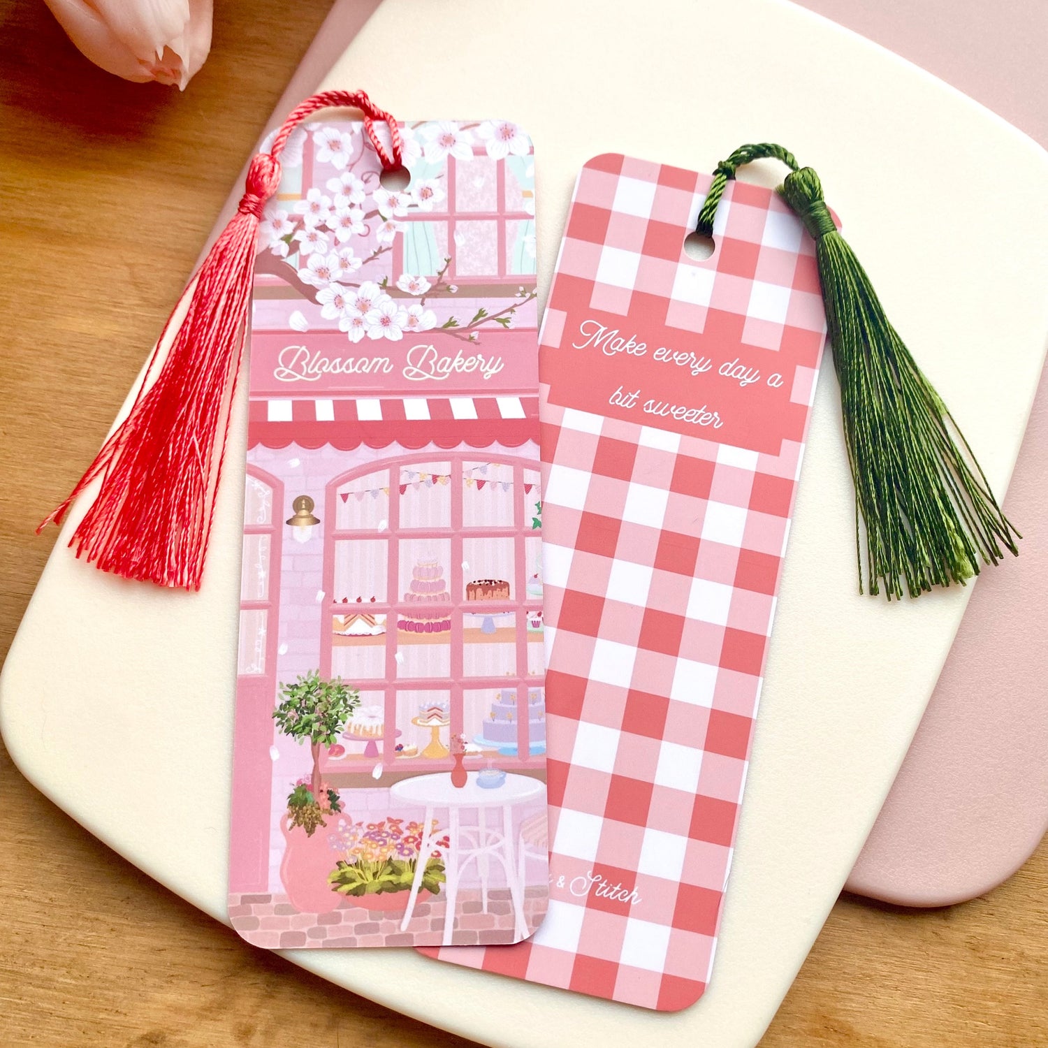 Two matching bookmarks with one showing the front design of a pink blossom bakery illustration and the other showing the back design with a pink gingham pattern