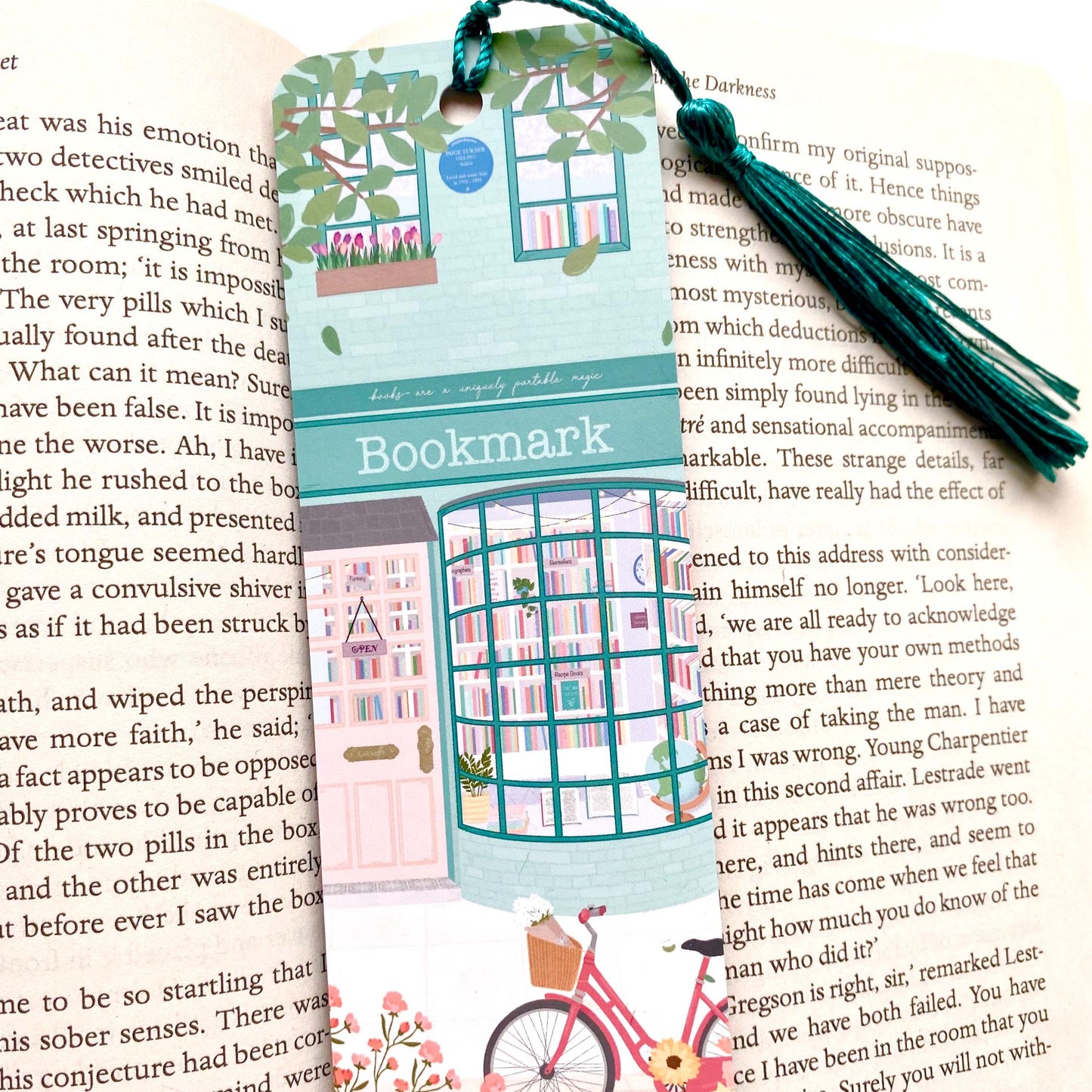 Decorative bookmark with a teal bookshop illustration and tassel on an open book