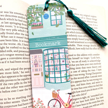 Decorative bookmark with a teal bookshop illustration and tassel on an open book