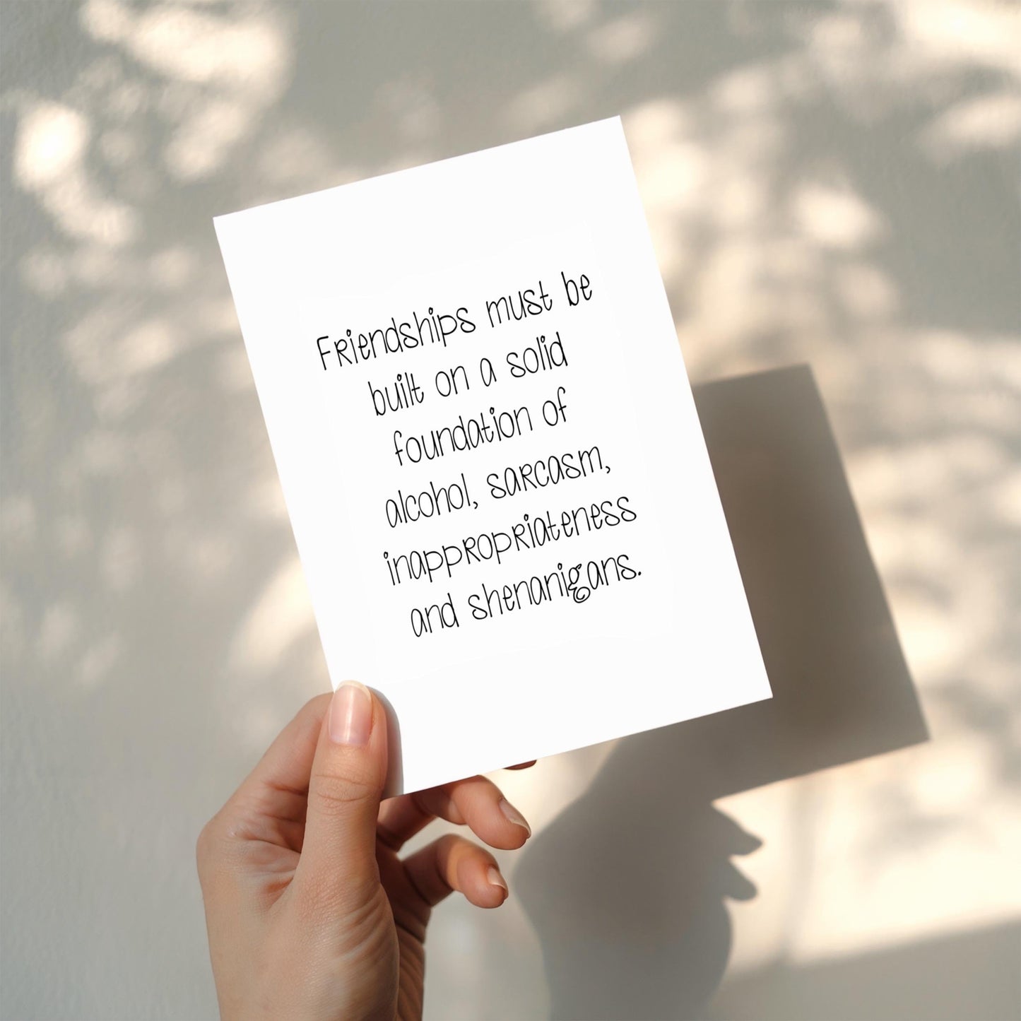 Hand holding a card with humorous friendship quote against a light background