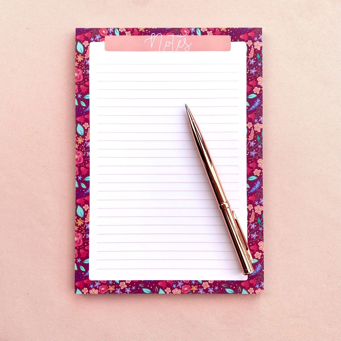 Floral notepad with a pen on a pink background
