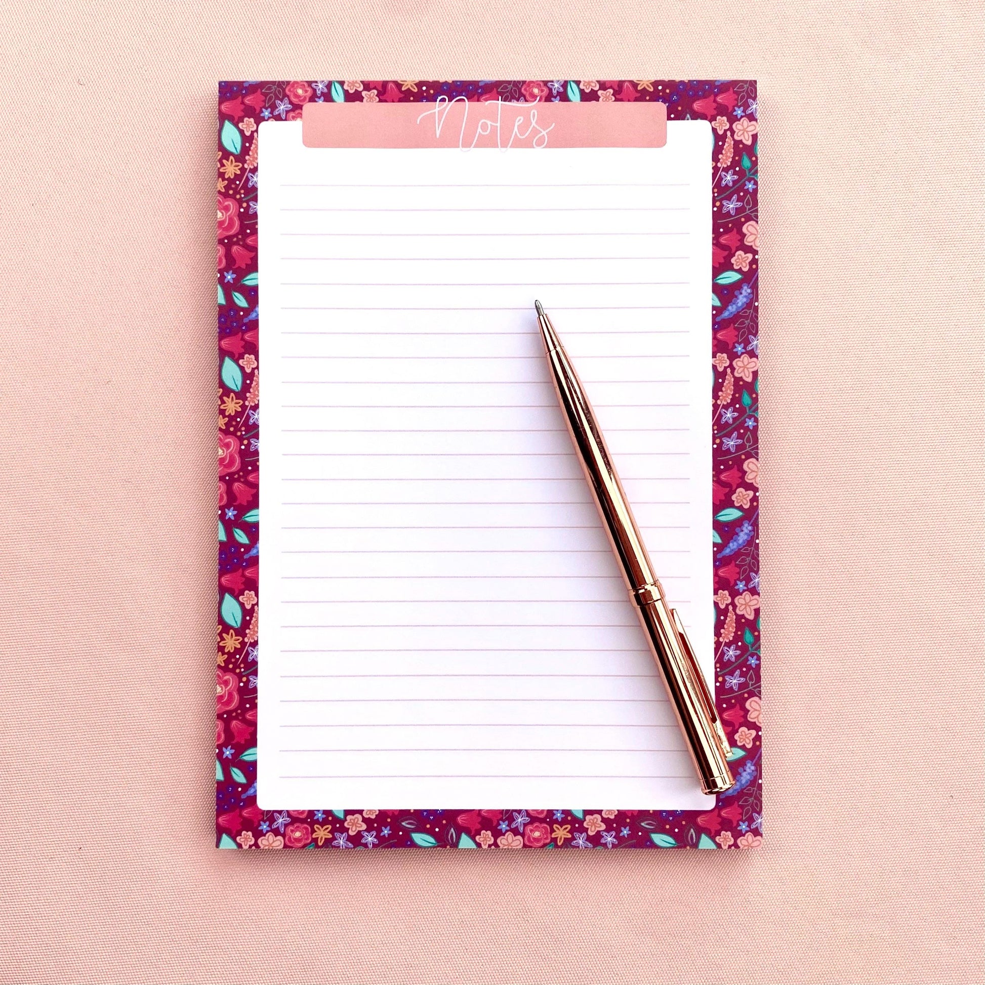 Floral notepad with a pen on a pink background