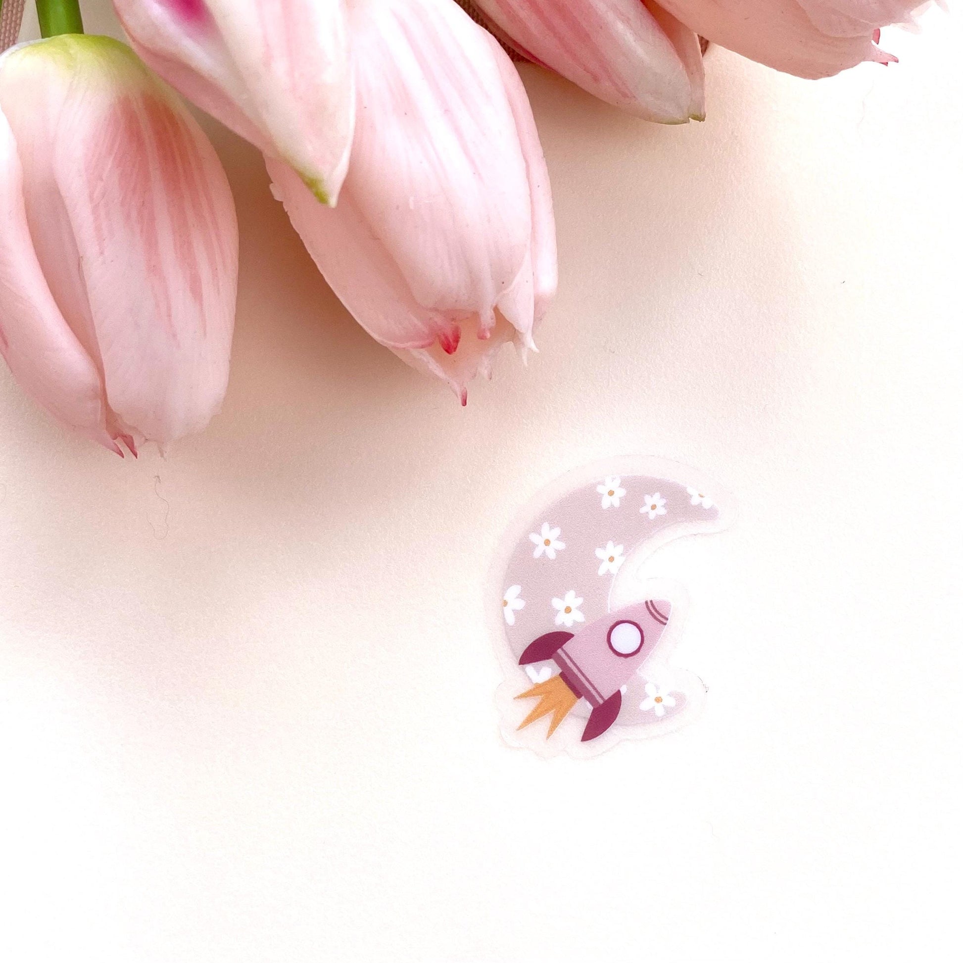 Decorative sticker with pink rocket and floral moon design on a white background