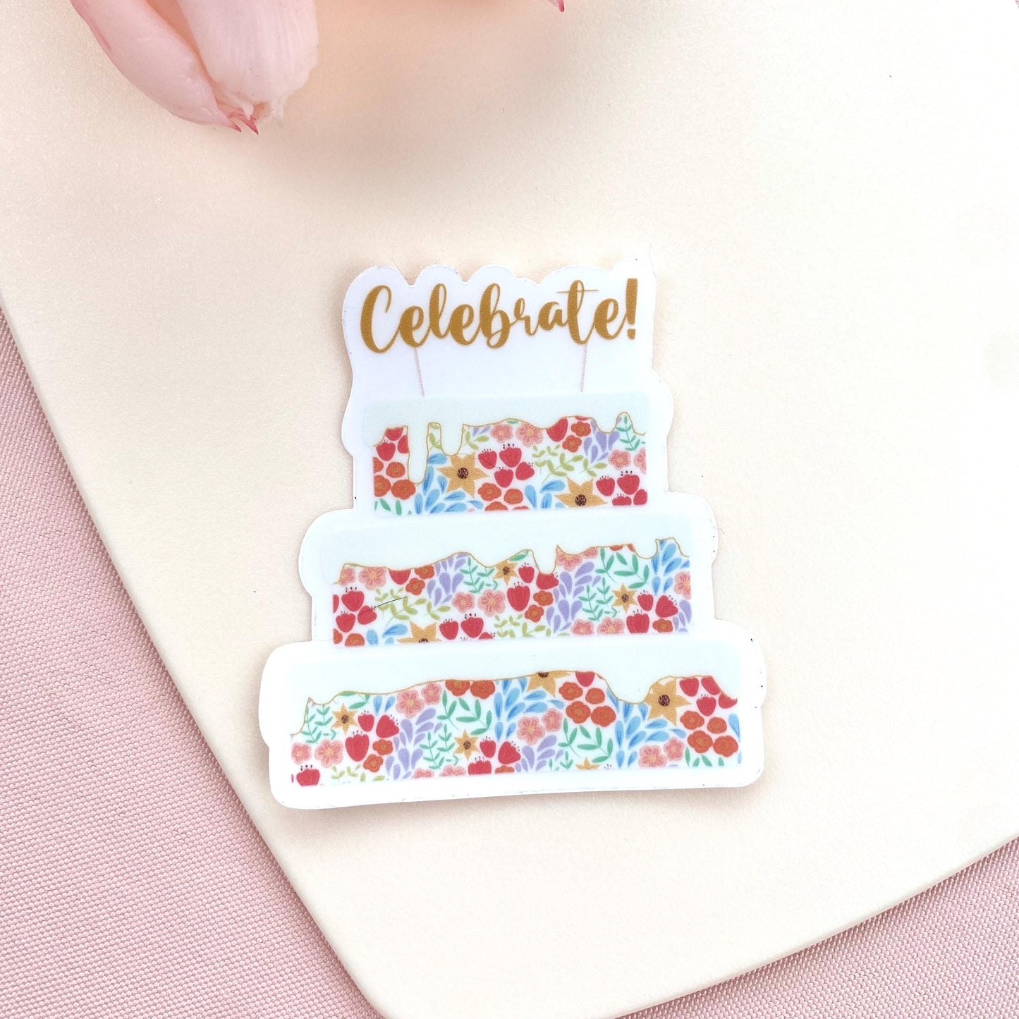 Decorative sticker with floral cake design and 'Celebrate!' text on a pink background
