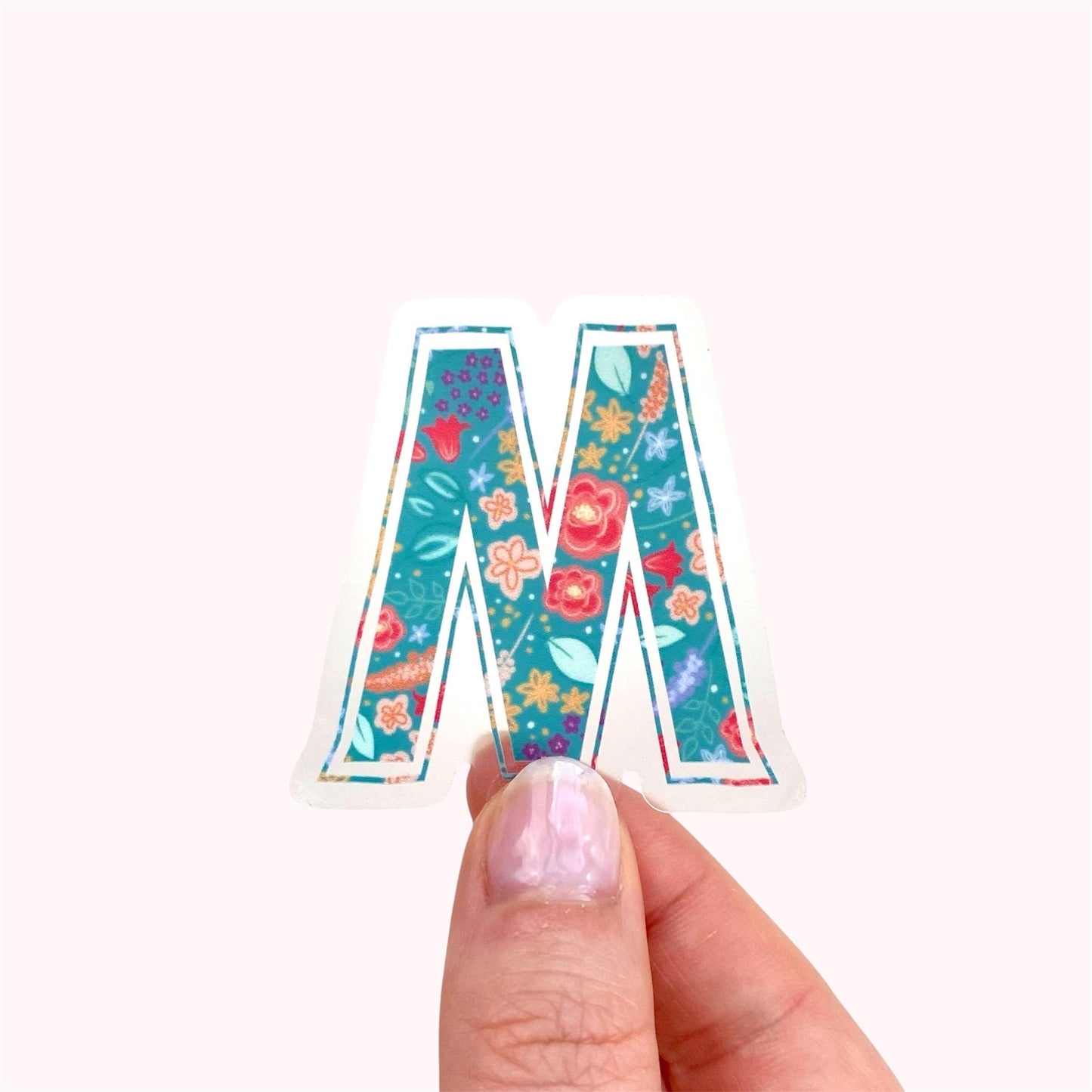 Colorful letter 'M' sticker held by a hand on a white background