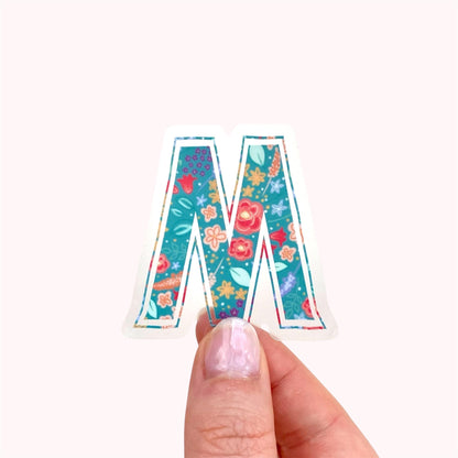 Colorful letter 'M' sticker held by a hand on a white background
