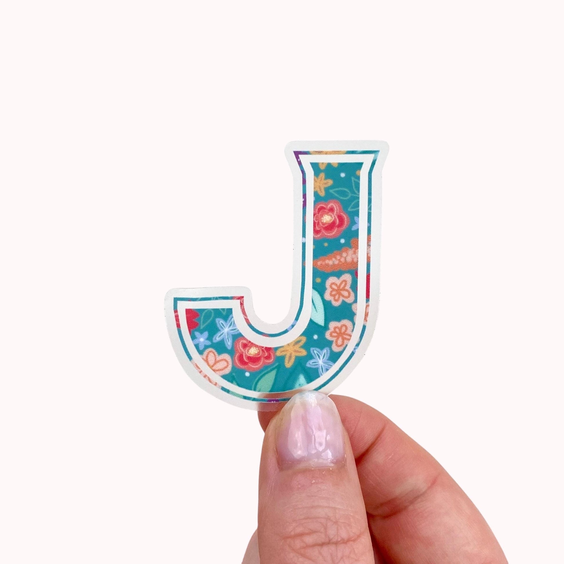 Colourful letter 'J' sticker held by a hand on a white background