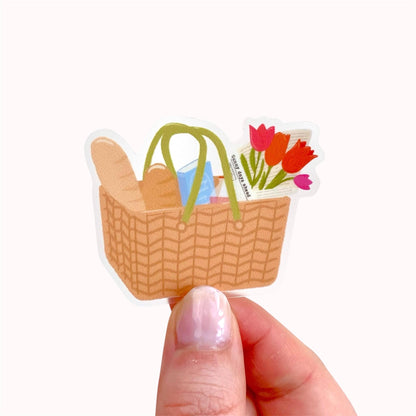 Sticker of a woven basket with flowers held by a hand on a white background