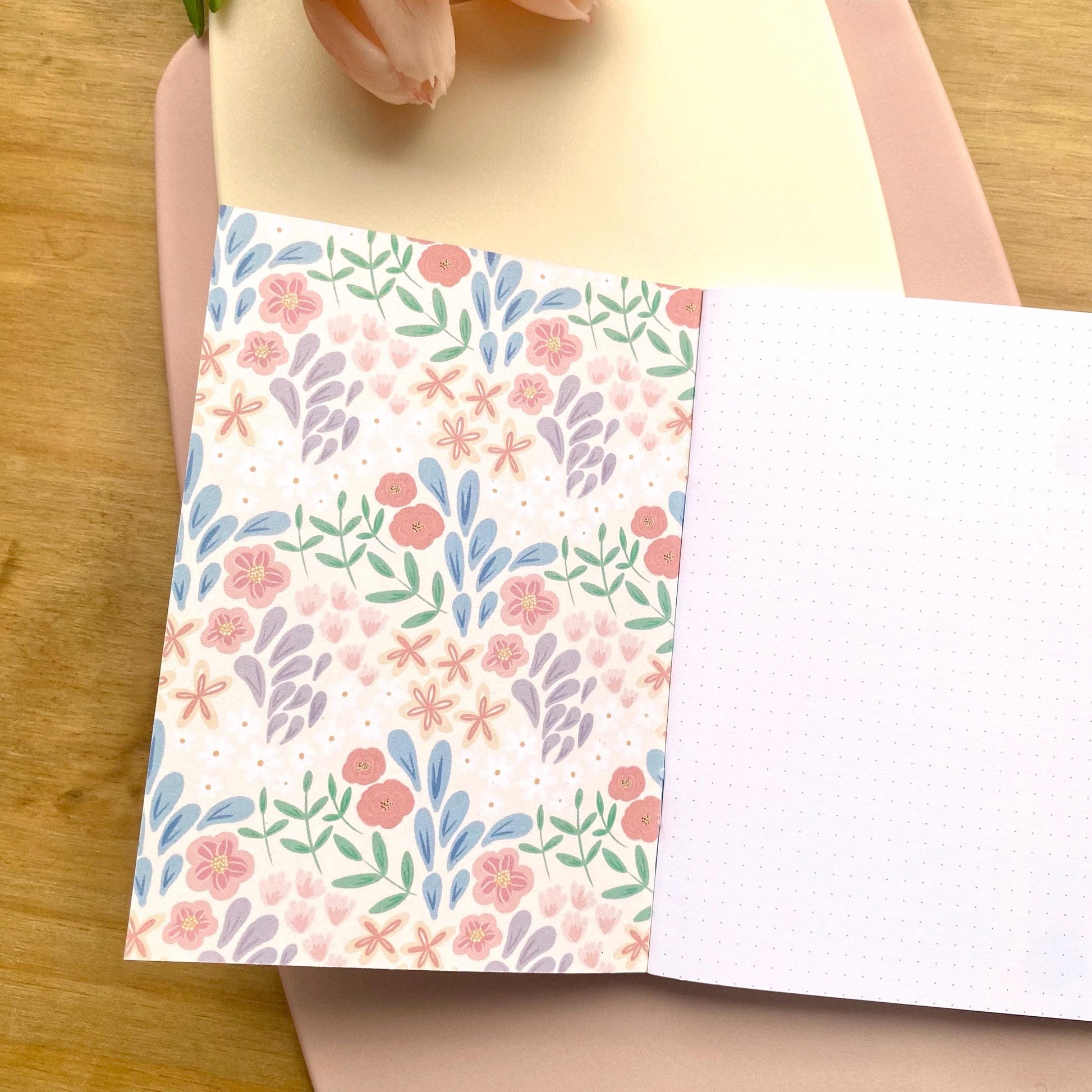 Floral patterned notebook on a wooden surface, open to show dotted inner pages