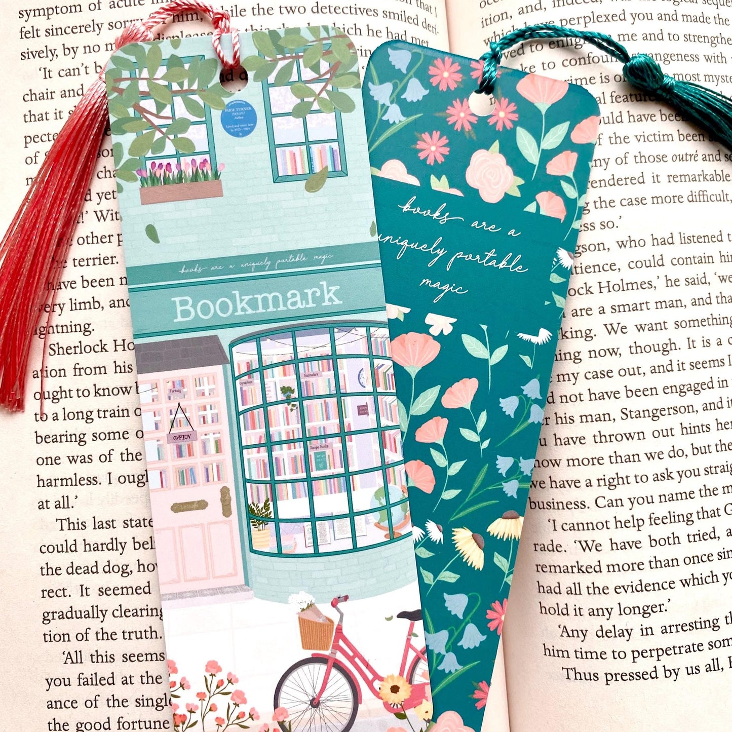 Two colourful bookmarks with tassels against an open book, one showing the front and the other showing the back
