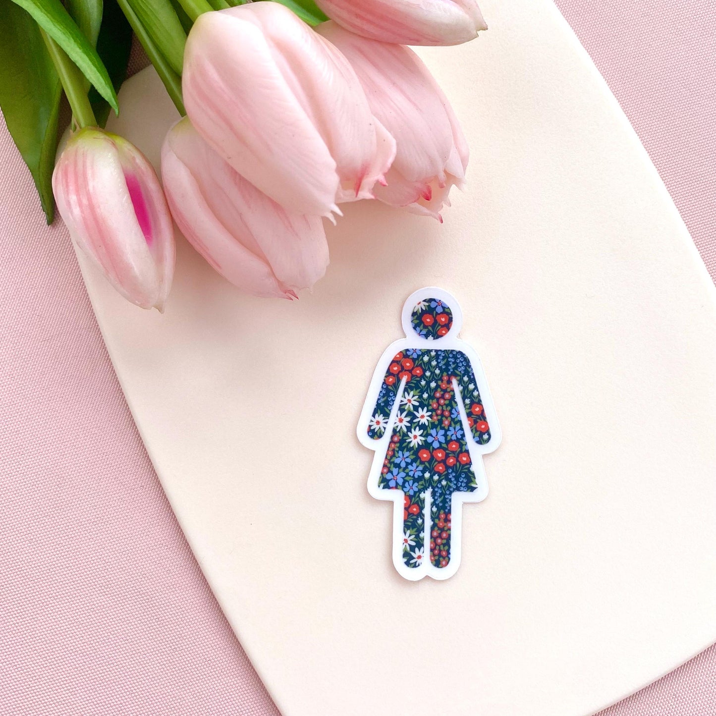 Floral-patterned woman symbol sticker on a pink surface with tulips