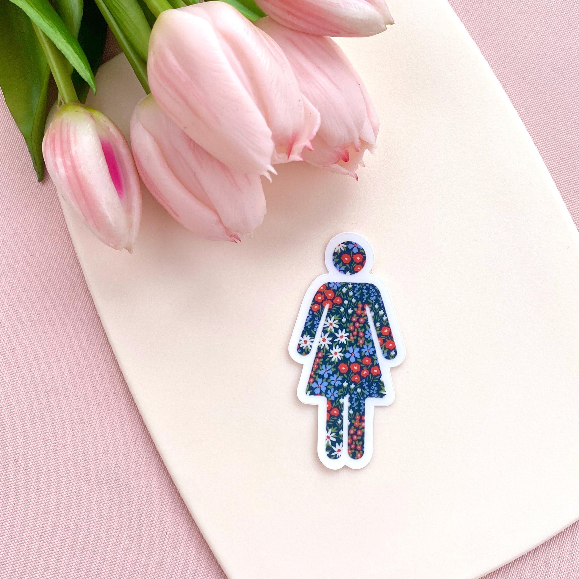 Floral-patterned woman symbol sticker on a pink surface with tulips
