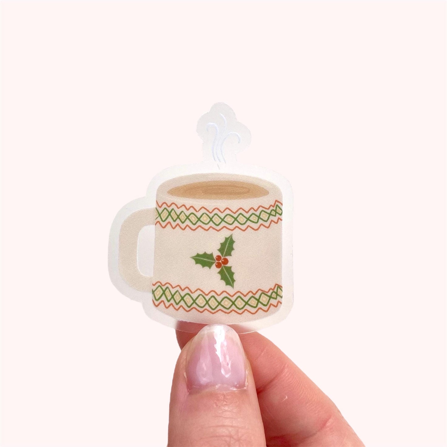 Small decorative mug sticker with holly design held by a hand on a white background