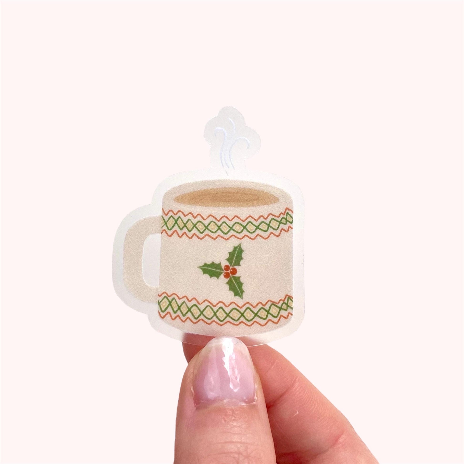 Small decorative mug sticker with holly design held by a hand on a white background