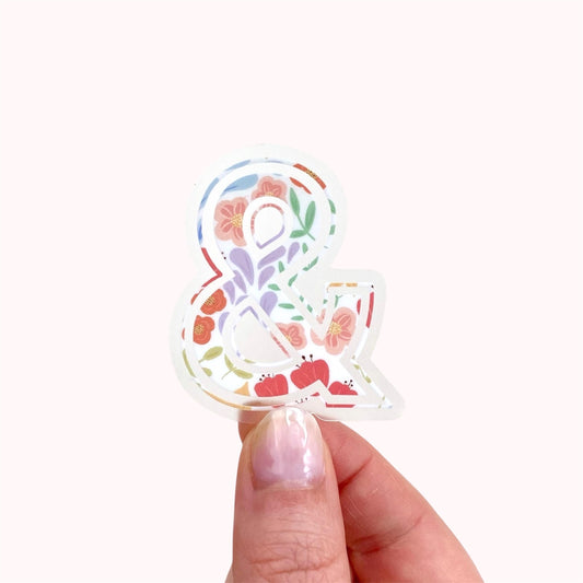 Hand holding a floral '&' symbol sticker on a white background