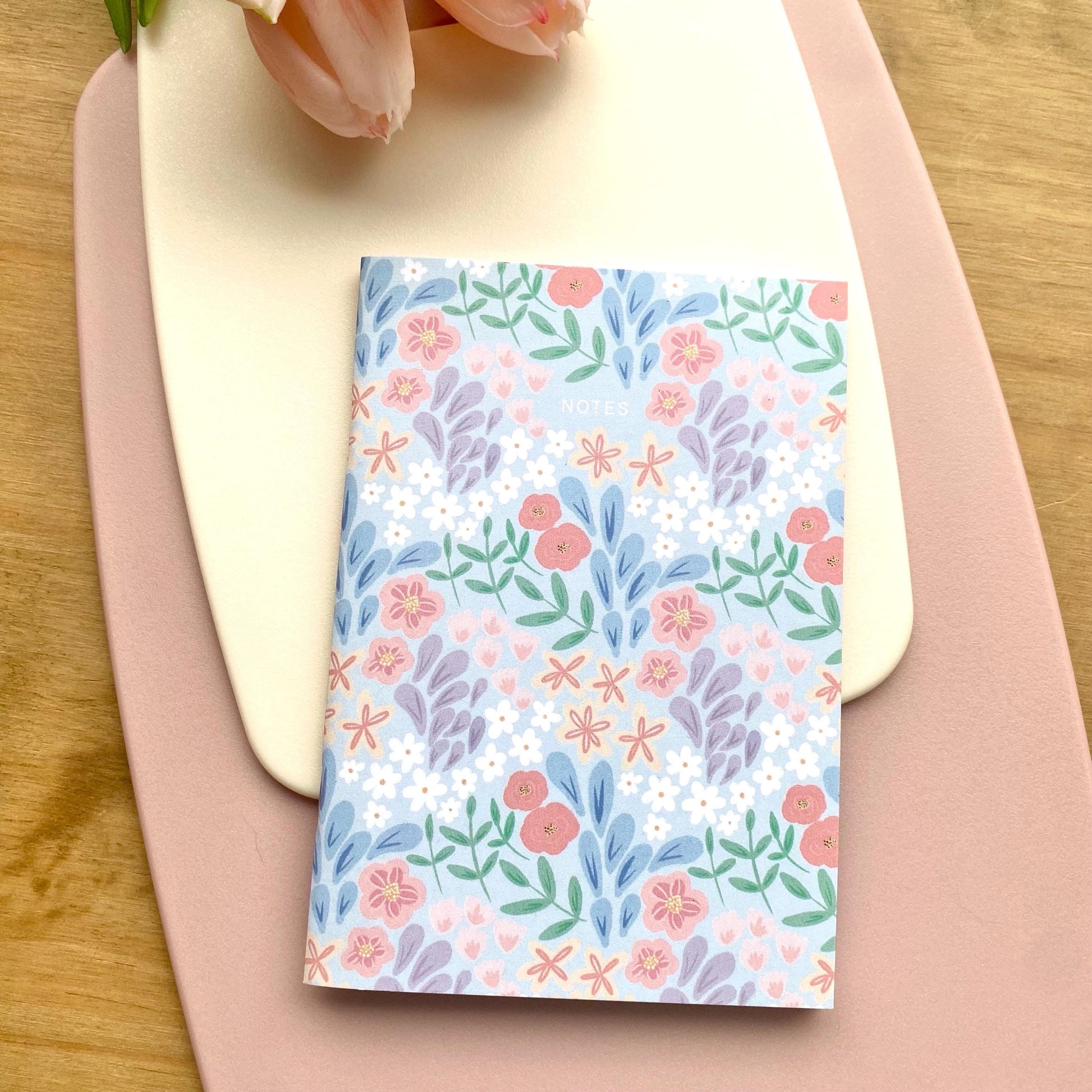 Floral patterned notebook on a pink surface with a wooden background