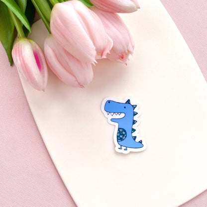 Blue dinosaur sticker on a pink surface with tulips