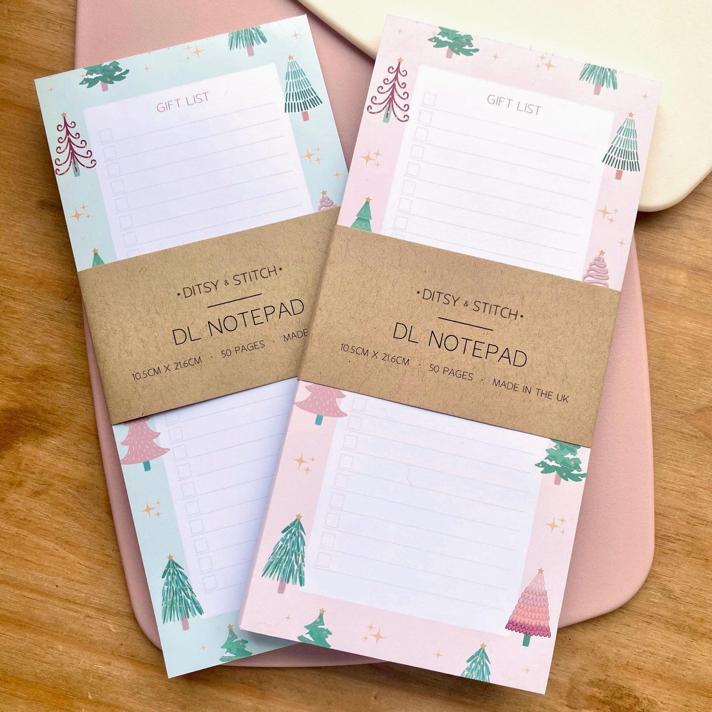 Two slim gift list notepads with Christmas tree designs on a wooden surface
