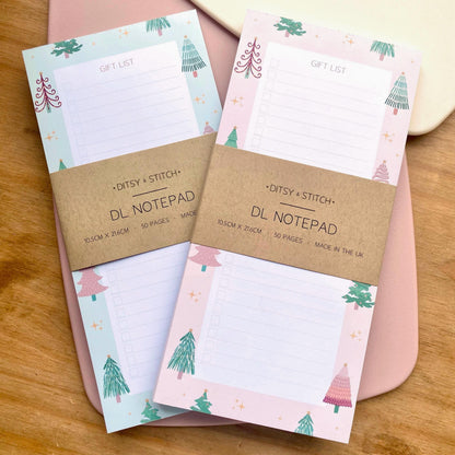 Two slim gift list notepads with Christmas tree designs on a wooden surface