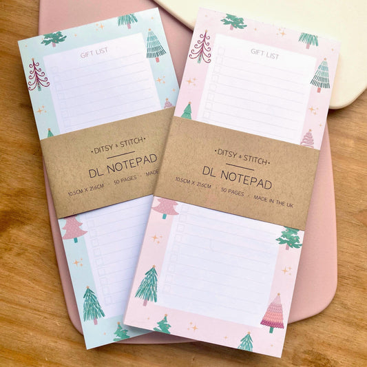 Two slim gift list notepads with Christmas tree designs on a wooden surface