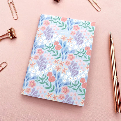 Floral notebook on a pink surface with a pen and paper clips.