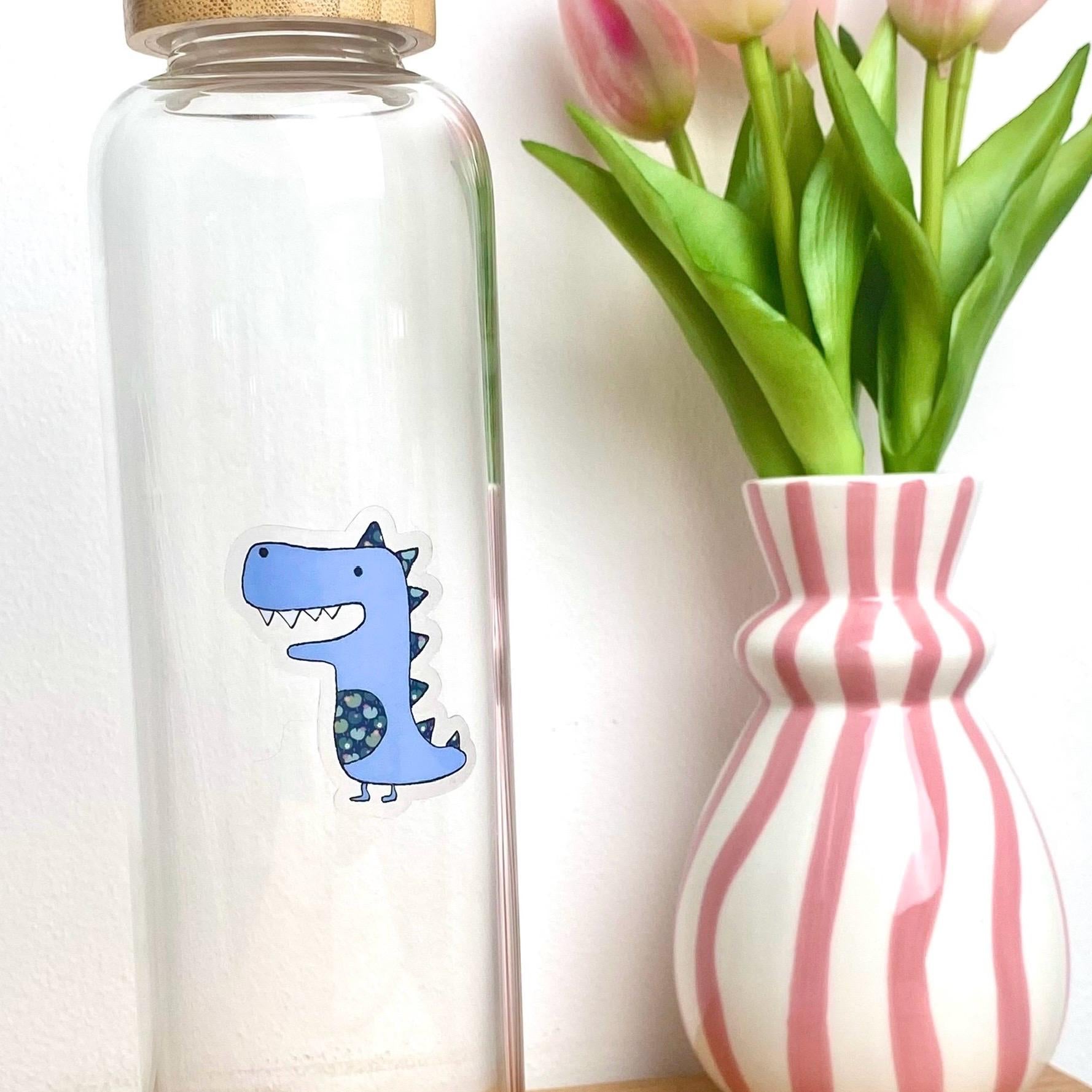 Clear glass bottle with a blue dinosaur sticker next to a striped vase with tulips